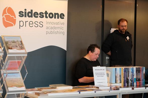 Two men behind a table full of books