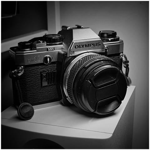 Olympus OM-10 slr camera sitting on top of a desk top speaker.