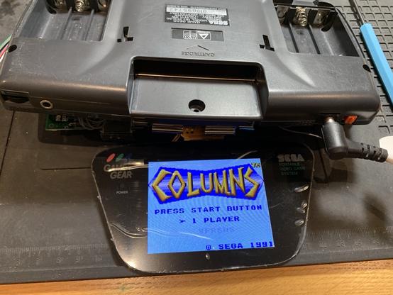 An LCD screen hanging out of a GameGear, partially disassembled. Columns title screen visible.