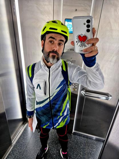 Fotografía en un ascensor. Selfie con el móvil en alto para conseguir un efecto de distorsión en la imagen. Llevo ropa de deporte muy colorida y un casco amarillo fosforito.