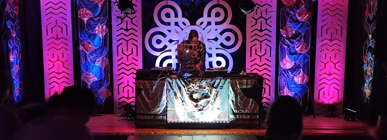Photo de l'artiste Mistikri jouant un live techno pour la retraite son silence et danse de dharma techno sur un fond de decoration de tissus créer par Debbie aka Feenix13 (spiral tribe) et panneaux bois decoupé a la cnc