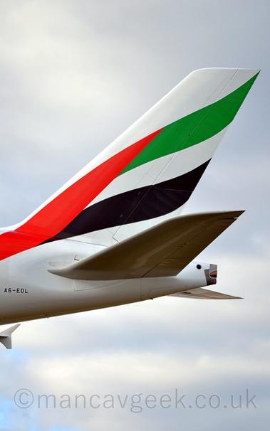 Close-up of the white rear fuselage and tail of a very large jet airliner flying from right to left at a low altitude.
There is a stylised, waving flag of the United Arab Emirates (red vertical stripe, then equal green, white, and black horizontal stripes) covering most of the tail, the red section extending down on to the rear fuselage.
The registration "A6-EDL" is visible on the lower rear fuselage, on the left of the frame.
The winglet on the end of the wing ion the other side of the plane is visible under the body on the left.
Cloudy white sky fills the rest of the frame.