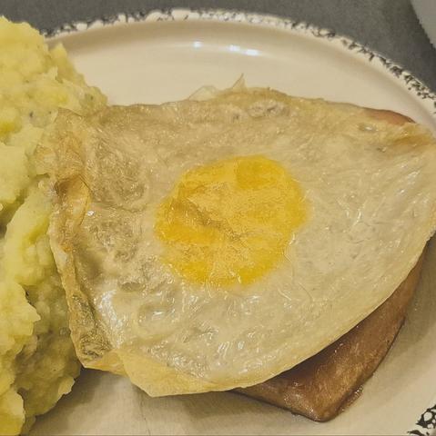 Ein veganes Spiegelei auf einem veganen Stück Leberkäse, daneben sieht man noch einen Berg Kartoffelbrei, der aber abgeschnitten ist. Das ganze auf einem beigen Teller.
