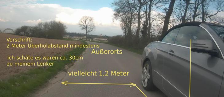 Fots einer Dashcam nach hinten. Ein Mercedes überholt mit ca. 30cm Abstand. 
Beschriftung: Vorschrift: 2 Meter Überholabstand außerorts. Ich schätze, es wren ca. 30cm zu meinem Lenker.