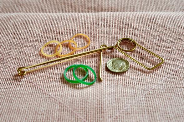An arrangement of yellow and green rubber bands, a brass wire toy, and a coin on a textured pink fabric background.