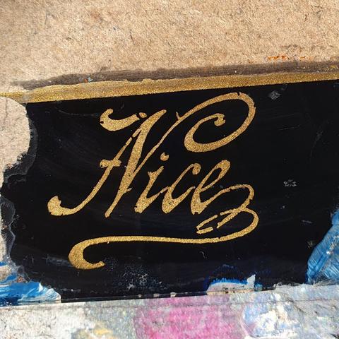 The word nice hand written in gold paint on a very dark blue background with flourishes circa 1929