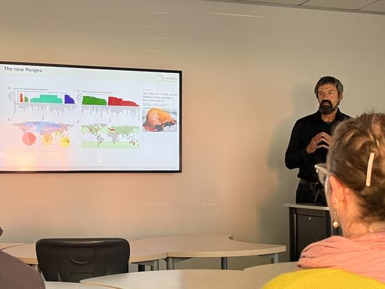 A photo of a bearded man, Prof. Franz Essl, and a presentation slide showing a map of the distinct communities of slugs and snails around the world. On the left are the native molluscs and the world is divided into many biogeographic regions. On the right are the naturalised (invasive) snails, and there's just a temperate and a tropic community.