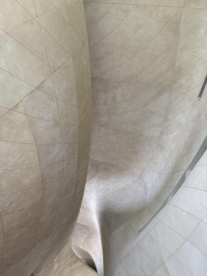 An abstract architectural interior featuring smooth, curved surfaces and subtle lines, creating a sense of fluidity and depth. The color palette consists of soft beige and light gray tones.