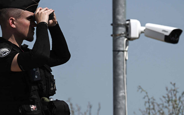 Gendarme regardant dans des jumelles, a proximité d’une caméra de surveillance.