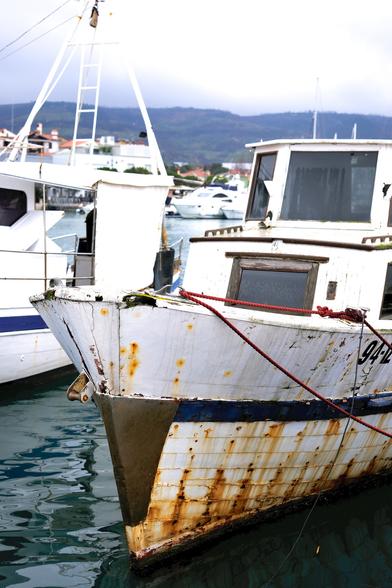 Motiv: 
Der vordere Teil eines alten Bootes. Es liegt in der Marina und rostet vor sich Hin. Die Planken haben bereits teilweise Löcher. Dahinter befinden sich Boote in weit besserem Zustand.

Stimmung und Wirkung: 
Das bedeckte Wetter unterstützt eine nostalgische Stimmung bei Betrachtung des Bootes, das seine besten Jahre bereits hinter sich gebracht hat.

Technische Detaiils:
Die Aufnahme ist von schräg rechts gemacht. Die Farben sind kräftig, womit das braun des Rosts noch stärker hervorgehoben wird und im Gegensatz zum Blaugrün des Wassers bzw. Himmels steht.