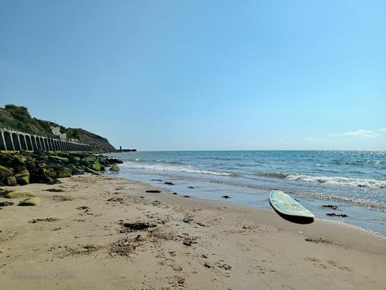 an abandoned surfboard lies on sunny sands beach in Folkestone