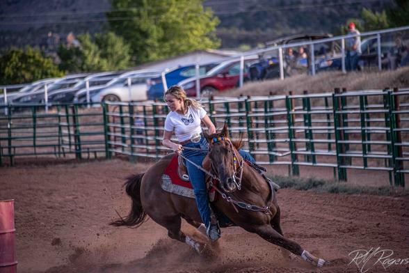 Photograph of a young woman competing in a rodeo's barrel race. She's turning her horse tightly around an obstacle.