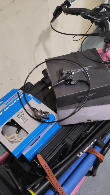 Sur la caisse d'un vélocargo rose, deux boîtes des disques de frein ainsi que deux boîtes de freins Shimano XT