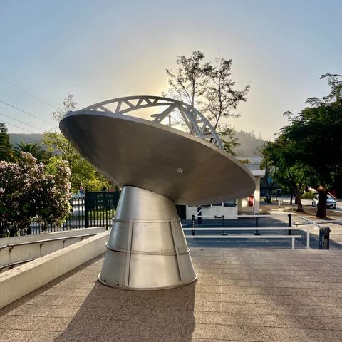 One of the flame cauldrons for the 2023 Panamerican Games in Santiago sitting at the entrance of the ESO and ALMA offices, backlit by the sun. The secondary support arms converge on the setting sun.