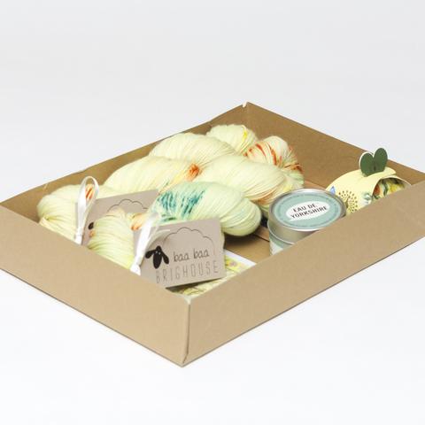 Picture shows an open A4 box containing two skeins of yarn in shades of lemon with yellow, orange and green speckles. A tin candle can also be seen. The rest of the box contents is obscured by the sides of the box.