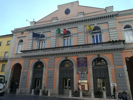 The image appears to show a building that features a classic architectural style, likely a theater given the presence of the word "Teatro" in the name. The facade is adorned with flags, including the European Union flag and the Italian flag. The structure has decorative elements such as arches, columns, and a prominent entrance. It may also have a banner or poster displayed outside, suggesting ongoing events or performances. The color scheme includes pastel tones, giving it a distinctive appearance.

Image Credits: Wikimedia / Redshift87 / CC BY-SA 4.0