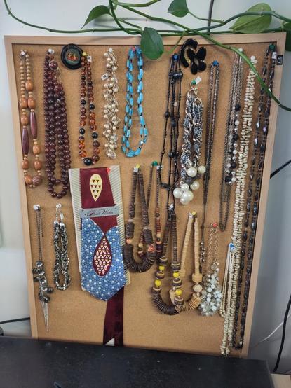 a peg board with lots of necklaces and a tie in the middle