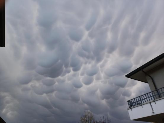 Cielo completamente coperto di nuvole grigie. L'aspetto è quello di una distesa di bitorzoli tondeggianti rivolti verso il basso. Una casa spunta sulla destra.