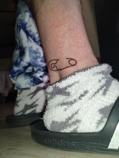 black line art tattoo of a safety pin over my ankle, appearing to hold my fibula in place.