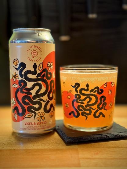 A can of beer that reads Les Intenables Craft Beer - Vices & Vertus pastry sour with rhubarb and tonka. The can is next to a matching half-height glass, with both featuring vector artwork of snakes on them with flower petals amongst them.