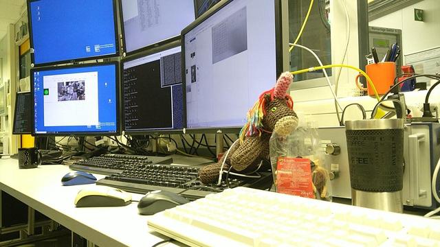 Max, das bunte Strickhorn, schaut in eine Trockenfruchtmischungspackung; im Hintergrund etwas Monitorwand vom Röntgenmikroskop.