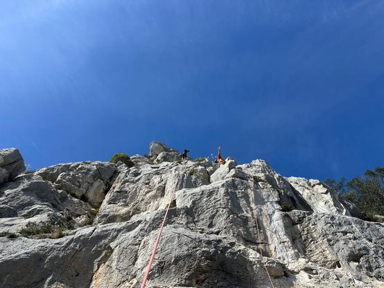 Top! two climbers at the top of a limestone cliff, framed against a blue sky