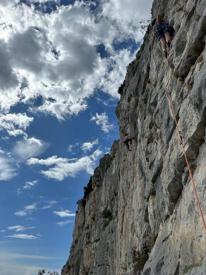 A climber on a limestone wall, cloudy sky above the crag, top right to bottom left