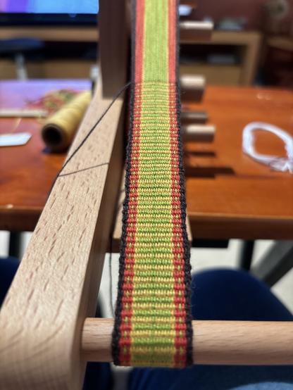 Woven band in brown, red orange, lime green and gold on an inkle loom.