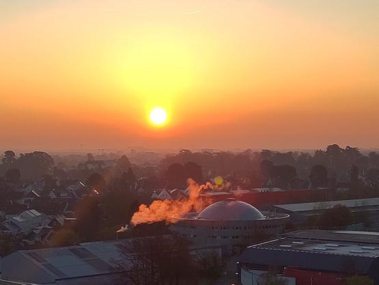 lever de soleil zoomé sur la ville avec un bâtiment qui fait de la fumée qui est rouge a cause du lever de soleil