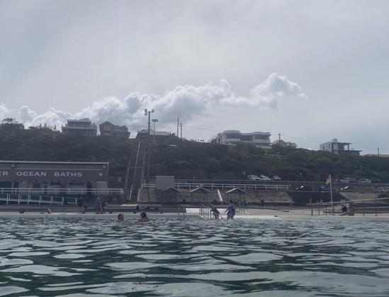 Looking up from the main pool at the baths towards a long white cloud shape on the top of the hill. Looks like a hidden steam train is running just behind the hill, puffing up smoke clouds. Maybe it's a sleeping dragon dreaming of its hoard.