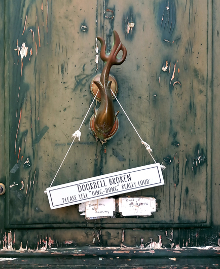 A brass dolphin door knocker at Villa Parisio in Lija, Malta. A sign hanging on the knocker says: "DOORBELL BROKEN. PLEASE YELL "DING-DONG" REALLY LOUDLY".