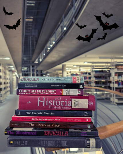 A stack of books on fictional vampires in film and English literature, as well as a book about libraries in fiction lies on a bannister in SUB Göttingen. The background shows a dark night sky outside of the windows, with little cartoon bats photoshopped in the background of the library rooms