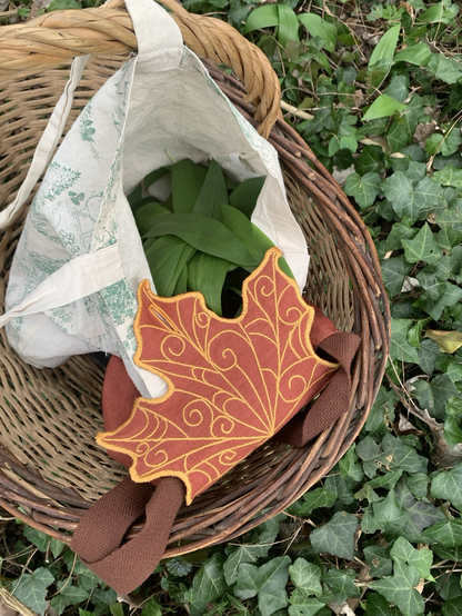 Sac feuille brodée orange et jaune en lin, tote bag rempli de feuilles d’ail des ours, dans un panier, fond de lierre au sol