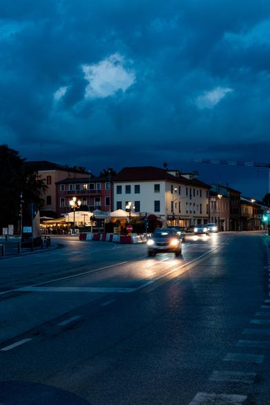 a road with three cars in the blue hour. Dramatic blue sky. In the background are some houses