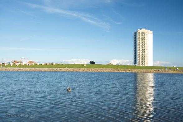 A stand-alone tower block is reflected in the water