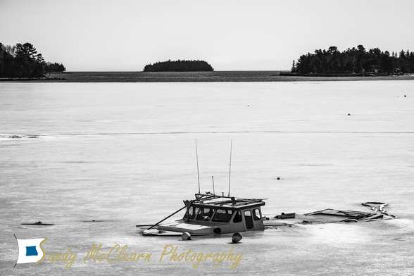 Cabin of a sunken boat protruding from the ice of a bay with an island on the horizon.