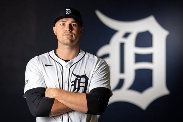 Tarik Skubal poses in a white Detroit Tigers jersey with a large Detroit Tigers logo in the background.