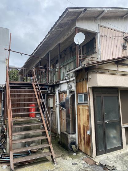 An old apartment sits with a long staircase leading up. The metal and wood of the building is worn in a rather pretty way.
