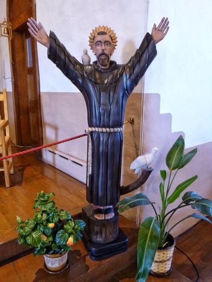 A statue of Saint Francis in a folk style, arms outstretched over his shoulders, with a couple of small animals attending.