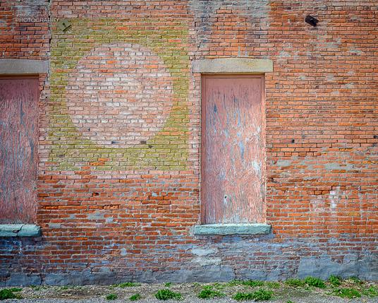 The outside of an old brick building with boarded up windows and the faded remains of a painted sign.