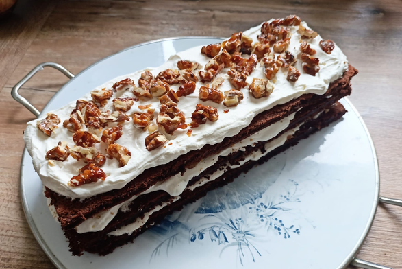 ein rechteckiger Kuchen wie beschrieben gefüllt. man sieht die dunklen Böden und die weißen Creme-Schichten, obendrauf karamellisierte Walnüsse