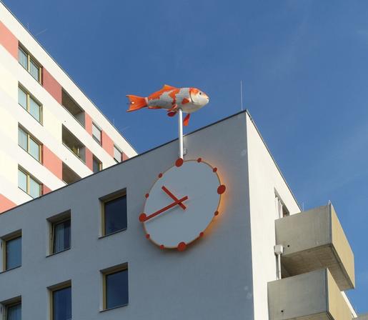 Gebäude mit Wanduhr, an der ein darübersituierter vom WInd gesteuerter Fisch hängt. (Kunstwerk "Winduhr oder Das Leben ein Hauch" von Alfredo Barsuglia)
