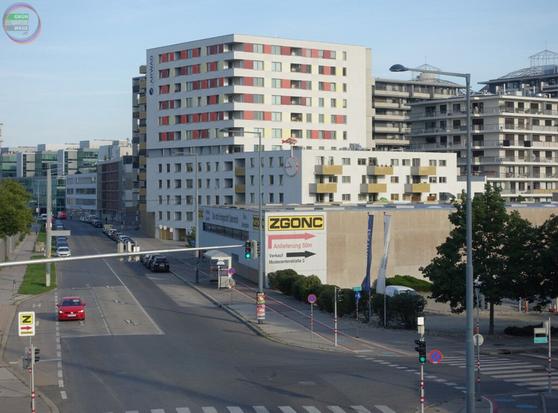 Blick von Steg auf kleinteilige heterogene Stadtrandstruktur mit Straße, Radweg, Einfamilienhaus, Baracken, Gasometer und drei Hochhäusern
