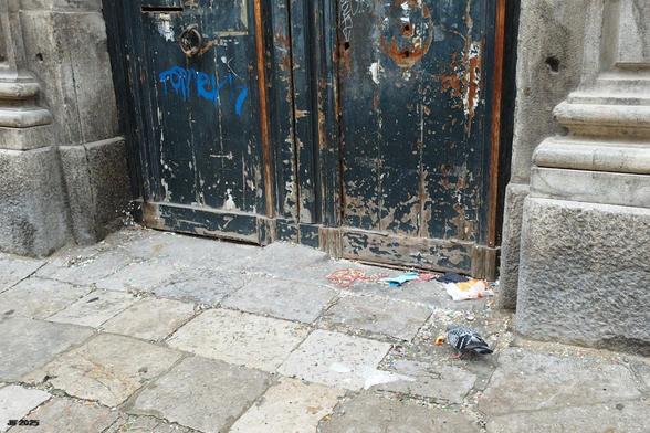 Farbfoto, aufgenommen in einer Straße von Palermo, Sizilien. Auf dem Pflaster vor einer verwitterten grünen Holztür hat eine Taube etwas Gutes zum Essen gefunden.