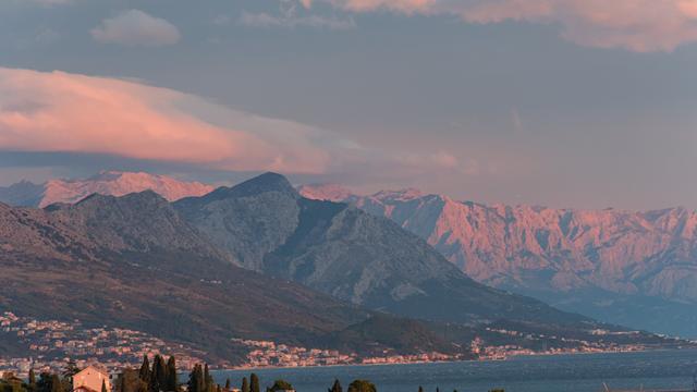 Rotes Abendleuchten auf Bergen im Hintergrund. Rechts ist Wasser zu sehen, an der Küste zwischen den Bergen und dem Meer sind ein paar Siedlungen.