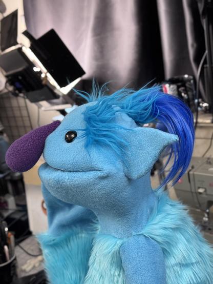Side view of a blue ogre live hands puppet with blue topknot and purple nose