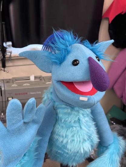3/4 view of a blue ogre live hands puppet with blue topknot and purple nose