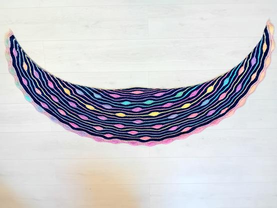 Photo d'un chale tricoté main. La couleur principale est le bleu canard. Il y a une alternance de rang arc en ciel, certains rangs comportent des gouttes.