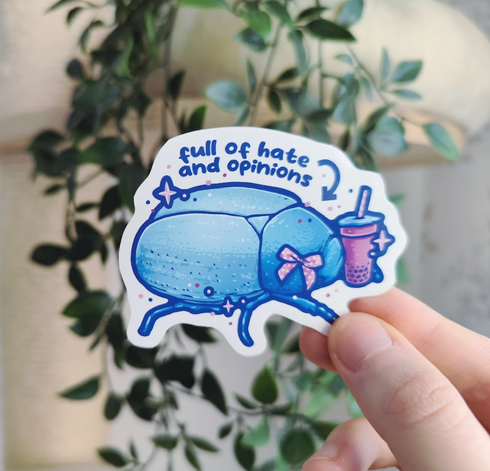 hand holding up a sticker of a blue bug wearing a ribbon and holding a boba tea, titled "full of hate and opinions"