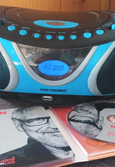 Auf der Anzeige eines kleinen, runden, azurblau-schwarzen Radios mit CD-Player steht die aktuelle Zahl für das Stück, das gerade gespielt wird - die 27. Vor dem Radio liegt, nur zur Hälfte erkennbar, eine CD mit dem Porträtfoto von Konstantin Wecker.